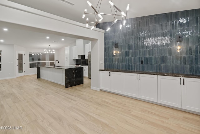 kitchen featuring visible vents, white cabinetry, backsplash, light wood finished floors, and an inviting chandelier