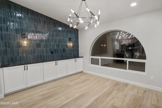 unfurnished dining area featuring baseboards, light wood-type flooring, an inviting chandelier, and recessed lighting