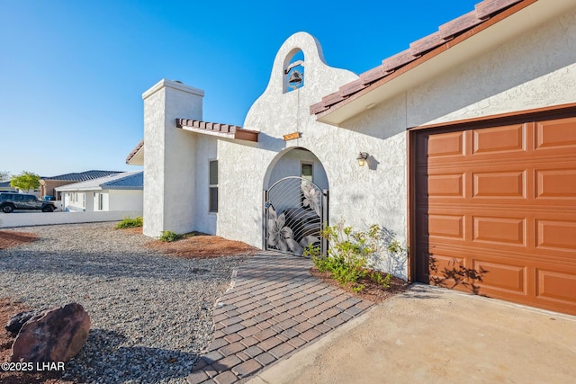 entrance to property featuring a chimney, a garage, and stucco siding