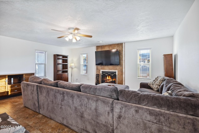 living room with a tiled fireplace, a healthy amount of sunlight, a textured ceiling, and a ceiling fan