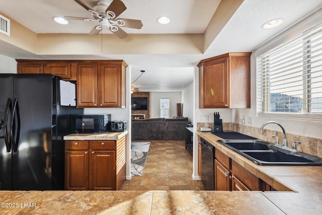 kitchen with brown cabinetry, a ceiling fan, a sink, black appliances, and light countertops