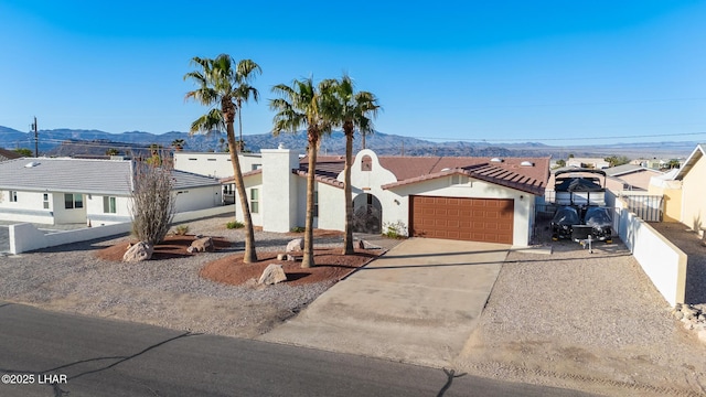 view of front facade with fence, an attached garage, a residential view, concrete driveway, and a mountain view