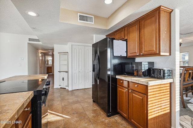 kitchen with visible vents, brown cabinets, black appliances, and tile counters