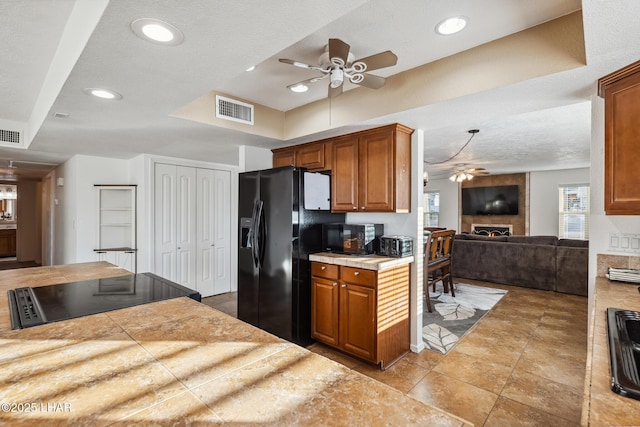 kitchen with visible vents, black appliances, brown cabinetry, a fireplace, and ceiling fan