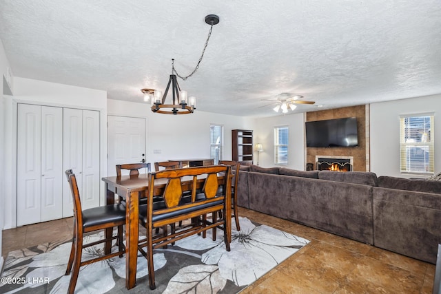 dining room with a large fireplace, a textured ceiling, and ceiling fan with notable chandelier