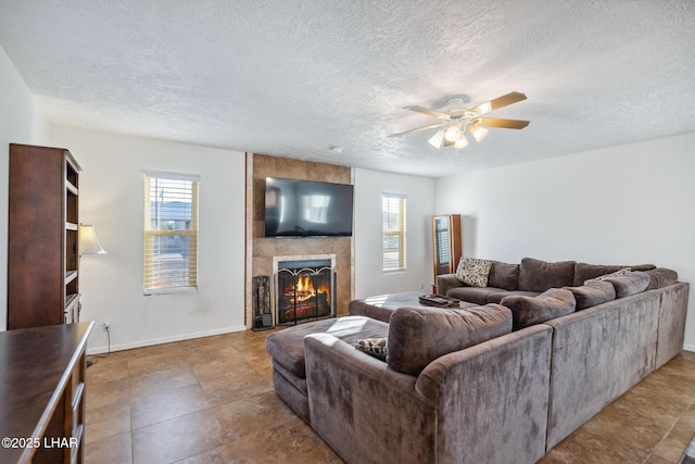 living room featuring ceiling fan, a textured ceiling, baseboards, and a tile fireplace