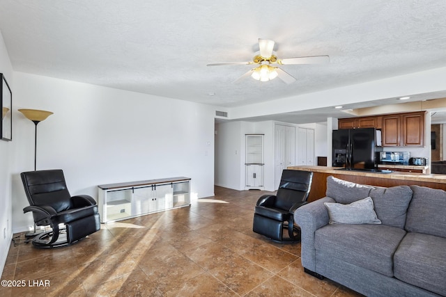 living room featuring a ceiling fan, visible vents, and a textured ceiling