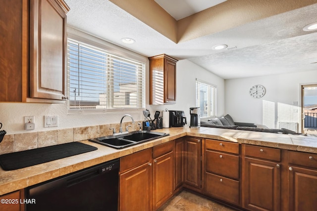 kitchen with brown cabinetry, a sink, a textured ceiling, dishwasher, and open floor plan