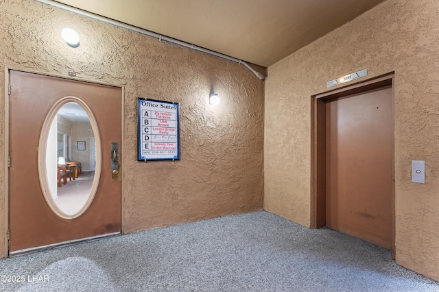 hall featuring carpet flooring, elevator, and a textured wall