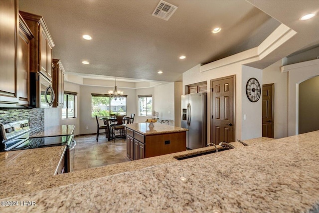 kitchen with sink, tasteful backsplash, a kitchen island, stainless steel appliances, and light stone countertops