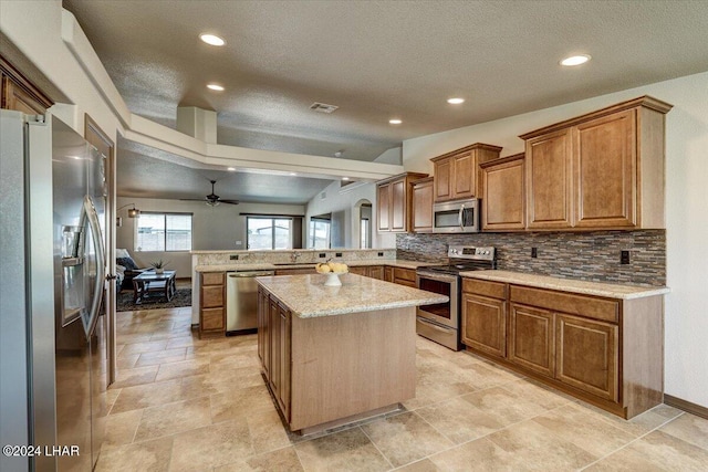 kitchen featuring appliances with stainless steel finishes, tasteful backsplash, light stone counters, a kitchen island, and kitchen peninsula