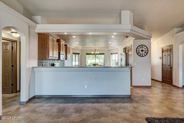 kitchen featuring appliances with stainless steel finishes, tasteful backsplash, light stone counters, kitchen peninsula, and an inviting chandelier