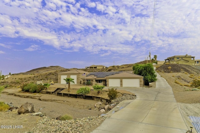 view of front of property with a garage, a mountain view, solar panels, and driveway