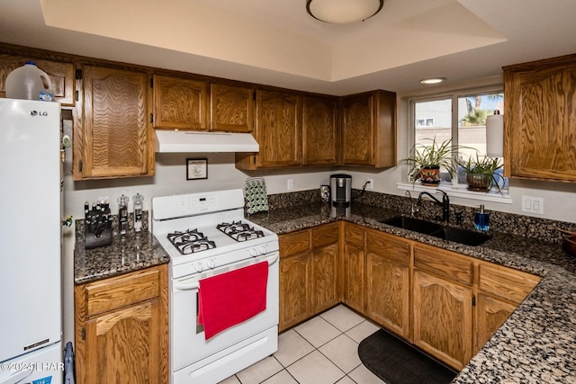 kitchen featuring sink, white appliances, dark stone counters, and light tile patterned flooring