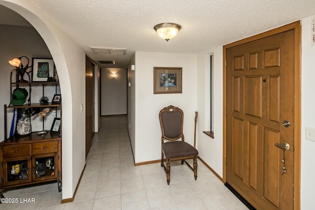 hall with a textured ceiling, light tile patterned floors, arched walkways, visible vents, and baseboards