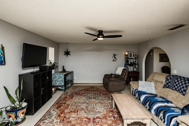 living area featuring arched walkways, light tile patterned floors, visible vents, ceiling fan, and a textured ceiling