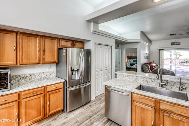 kitchen featuring lofted ceiling, sink, light hardwood / wood-style flooring, appliances with stainless steel finishes, and light stone countertops