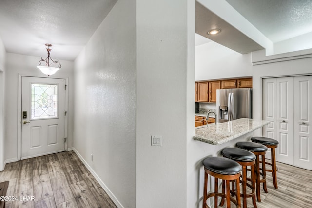 kitchen with decorative light fixtures, a kitchen breakfast bar, light hardwood / wood-style floors, light stone counters, and stainless steel refrigerator with ice dispenser