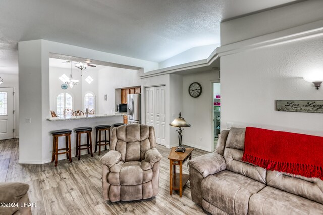 living room with an inviting chandelier, light hardwood / wood-style floors, vaulted ceiling, and a textured ceiling