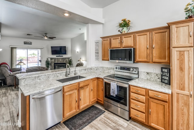 kitchen featuring sink, appliances with stainless steel finishes, kitchen peninsula, a fireplace, and light hardwood / wood-style floors