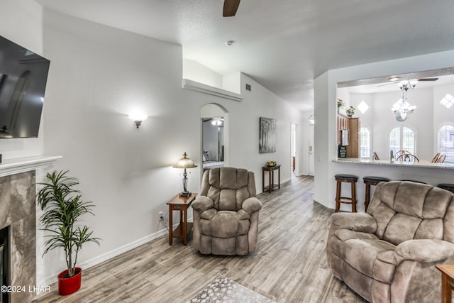 living room featuring lofted ceiling, ceiling fan with notable chandelier, a high end fireplace, and light hardwood / wood-style flooring