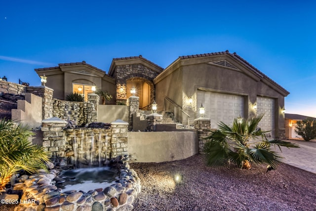 mediterranean / spanish-style house with decorative driveway, a tile roof, stucco siding, a garage, and stone siding