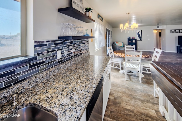 kitchen with a chandelier, dark stone countertops, dishwasher, pendant lighting, and decorative backsplash