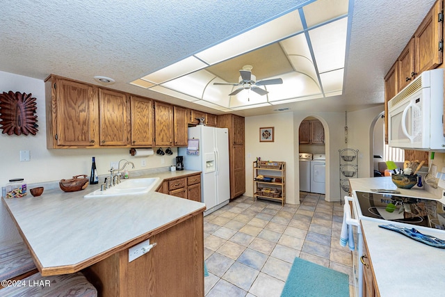 kitchen featuring kitchen peninsula, sink, washing machine and clothes dryer, a tray ceiling, and white appliances