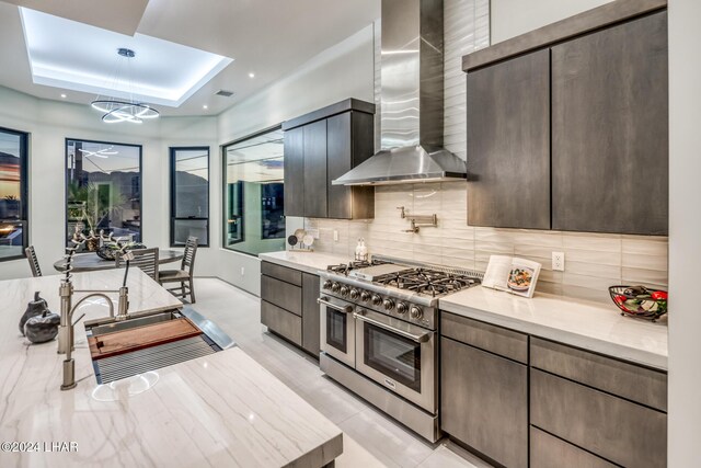 kitchen featuring wall chimney exhaust hood, tasteful backsplash, decorative light fixtures, a tray ceiling, and range with two ovens