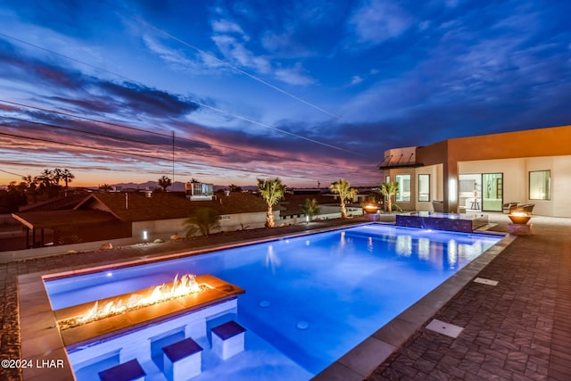 pool at dusk with a fire pit, a patio area, and pool water feature