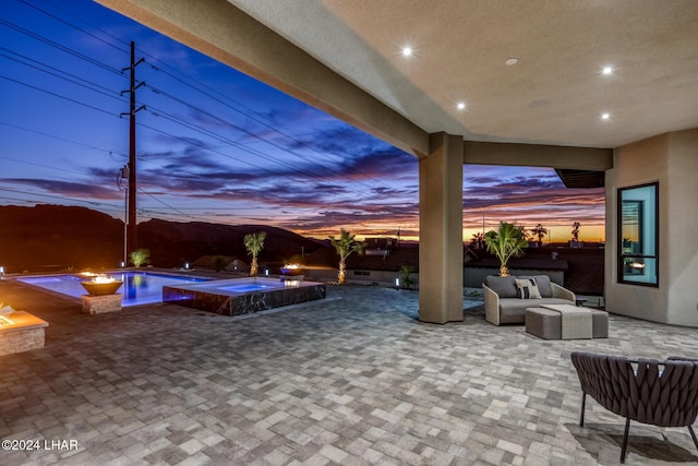 patio terrace at dusk featuring a pool with hot tub and an outdoor living space with a fire pit