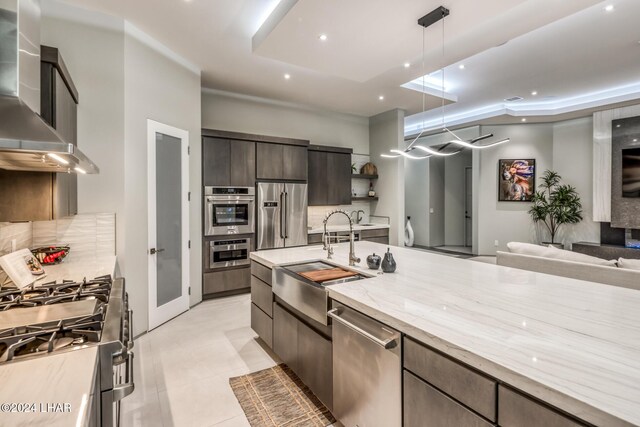 kitchen featuring wall chimney range hood, sink, hanging light fixtures, dark brown cabinets, and stainless steel appliances