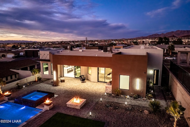 back house at dusk featuring a mountain view, an in ground hot tub, a patio, and an outdoor fire pit