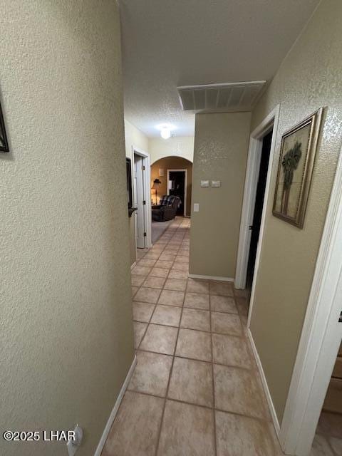 hall with visible vents, baseboards, light tile patterned floors, a textured wall, and arched walkways