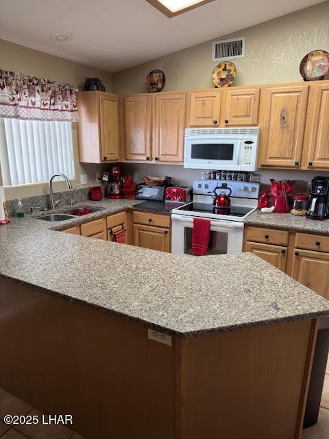 kitchen with white appliances, light stone countertops, visible vents, light brown cabinets, and a sink