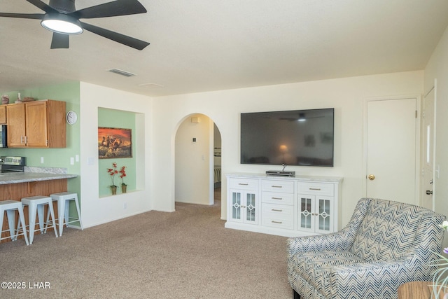 carpeted living area featuring arched walkways, visible vents, and a ceiling fan