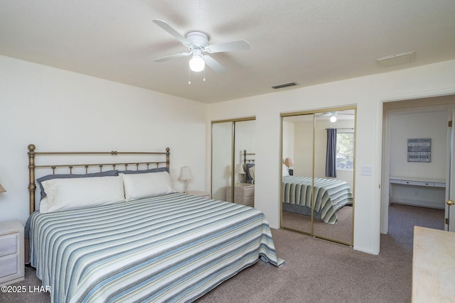 carpeted bedroom featuring visible vents, multiple closets, and ceiling fan