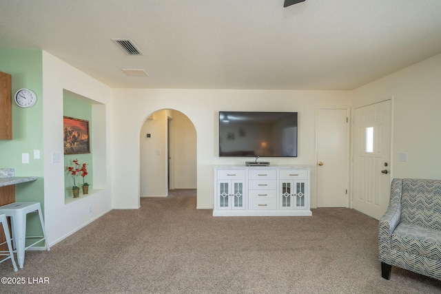 living area featuring visible vents, carpet, and arched walkways