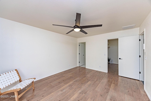 interior space featuring a spacious closet, light wood-style flooring, a textured ceiling, a ceiling fan, and visible vents