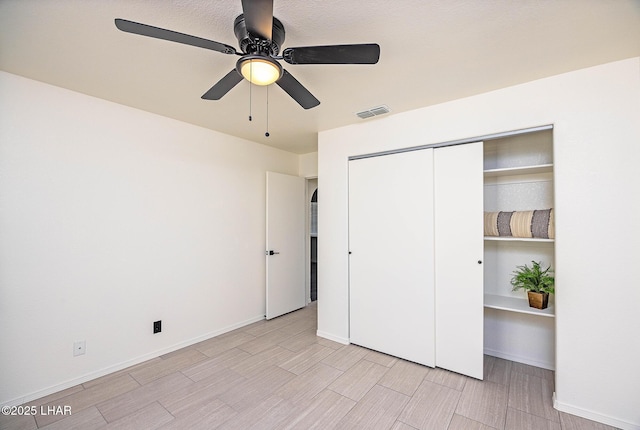 unfurnished bedroom featuring a closet, baseboards, wood finish floors, visible vents, and ceiling fan