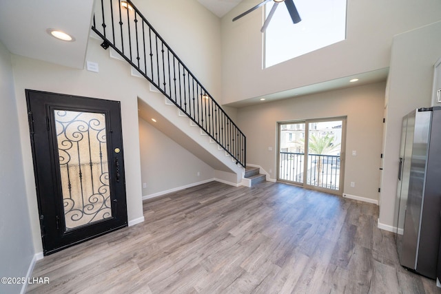 foyer entrance with a high ceiling, ceiling fan, and light wood-type flooring