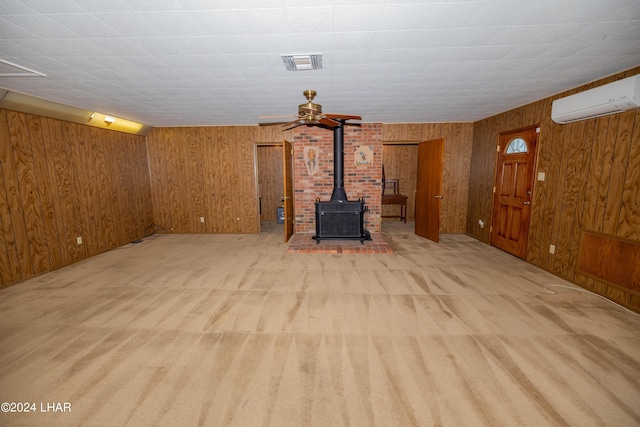 unfurnished living room with light carpet, an AC wall unit, wood walls, and a wood stove