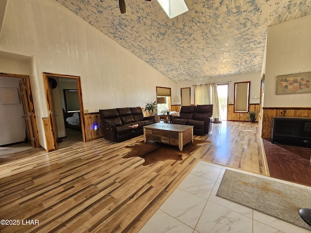 living area featuring wainscoting, a fireplace with flush hearth, marble finish floor, wood walls, and high vaulted ceiling