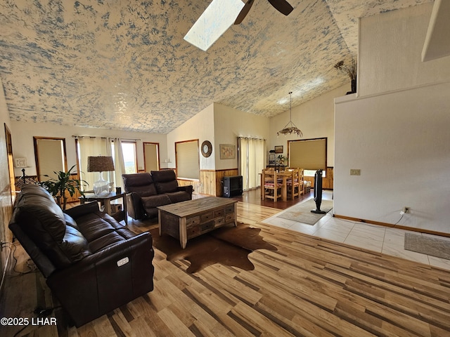 living room with a skylight, light wood-style flooring, high vaulted ceiling, and a ceiling fan