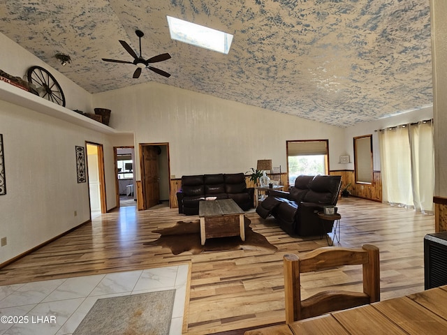 living room with a ceiling fan, a skylight, high vaulted ceiling, and light wood finished floors