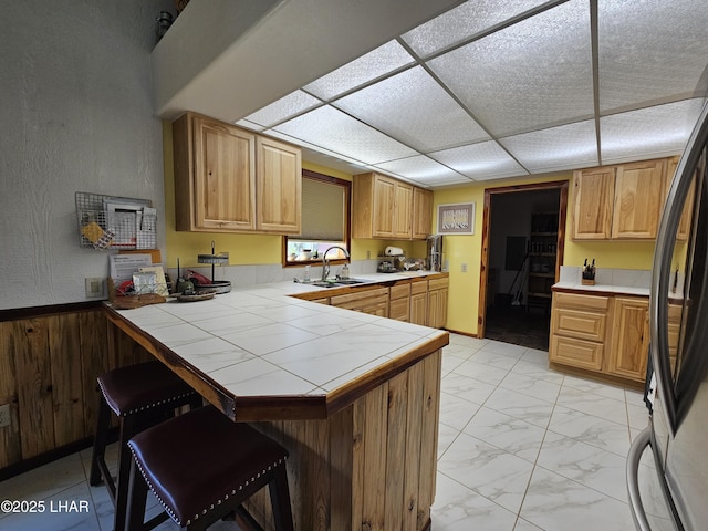 kitchen featuring tile countertops, a peninsula, a kitchen breakfast bar, marble finish floor, and freestanding refrigerator