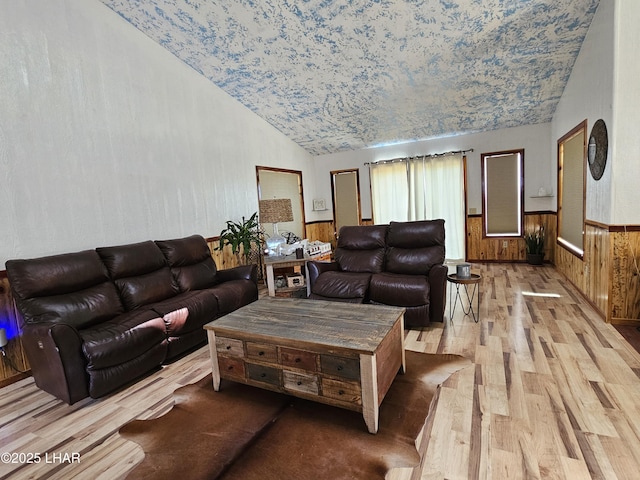 living room featuring lofted ceiling, wood walls, light wood-type flooring, and wainscoting