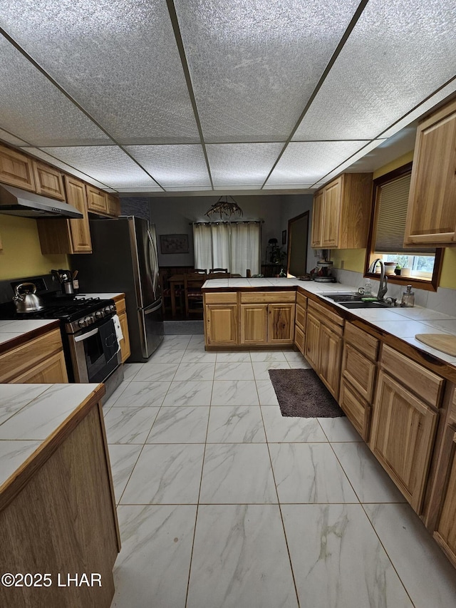 kitchen featuring marble finish floor, brown cabinets, stainless steel stove, a peninsula, and under cabinet range hood