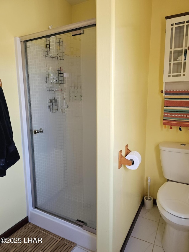 bathroom with a stall shower, tile patterned flooring, baseboards, and toilet