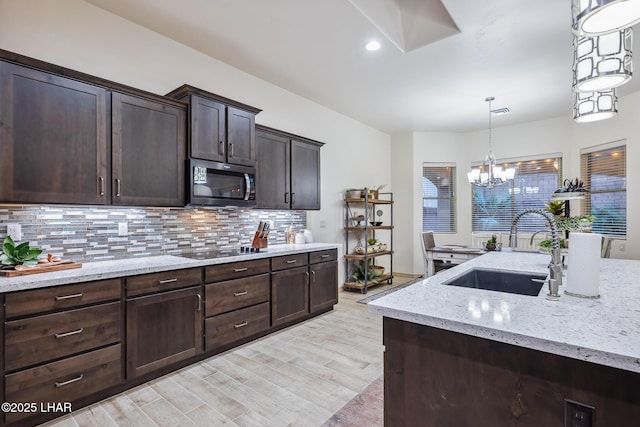 kitchen with black electric cooktop, a sink, stainless steel microwave, light wood finished floors, and decorative backsplash